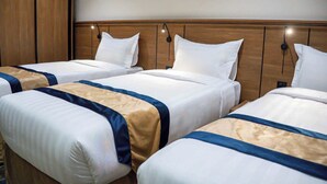Three single beds with white linens and blue and beige bedspreads, wooden headboards, and wall-mounted reading lights. - Rayan Al Jiwar Hotel (Makkah)