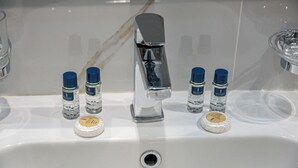 A bathroom sink with a chrome faucet, four bottles of shampoo, and two soap bars. - Rayan Al Jiwar Hotel (Makkah)