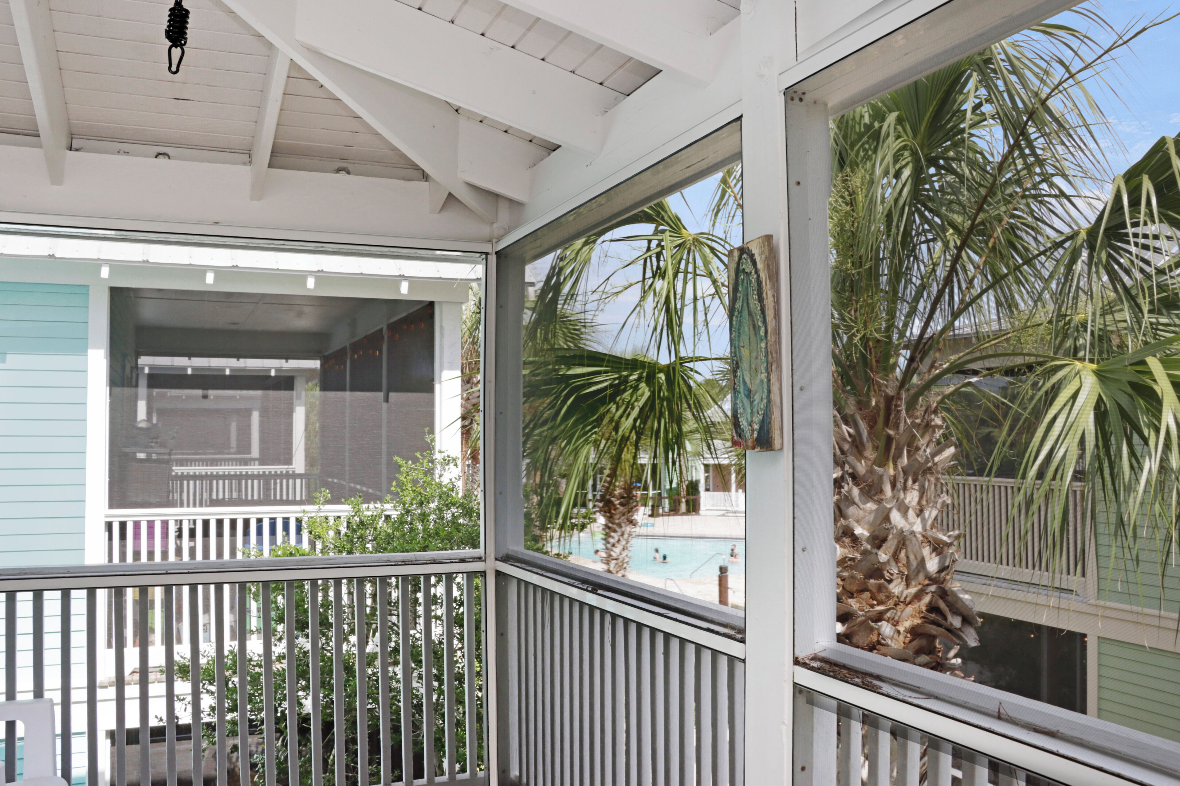 A covered porch with a railing, a view of a swimming pool, and palm trees.