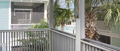 A covered porch with a railing, a view of a swimming pool, and palm trees.