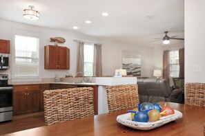 A kitchen with wooden cabinets, a dining table with wicker chairs, and a ceiling fan. - ☀️ Gated Community - 2 Pools - Barefoot Cottage B28 🌴 (Port St. Joe)