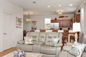 A living room with a gray leather sofa, a wooden coffee table, and a dining area with wicker chairs. - ☀️ Gated Community - 2 Pools - Barefoot Cottage B28 🌴 (Port St. Joe)