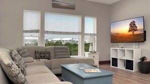Ein Wohnzimmer mit Sofa, Couchtisch, Fernseher und Blick auf Häuser durch große Fenster.