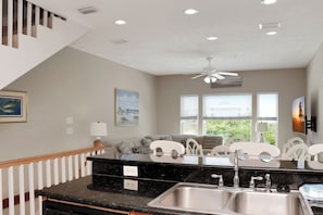 A kitchen with a black countertop, stainless steel sink, ceiling fan, and a view of the outdoors through large windows. - 🌴 Short Walk to Beach - Pet Friendly - Living the Dream ☀️ (Mexico Beach)