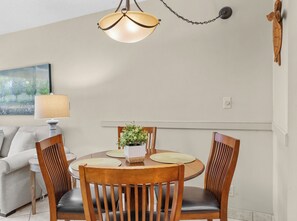 A dining area with a round table, wooden chairs, a potted plant, and a pendant light. - Maui Banyan G-105 | Lush Oasis + Steps to Beach! (Kihei)