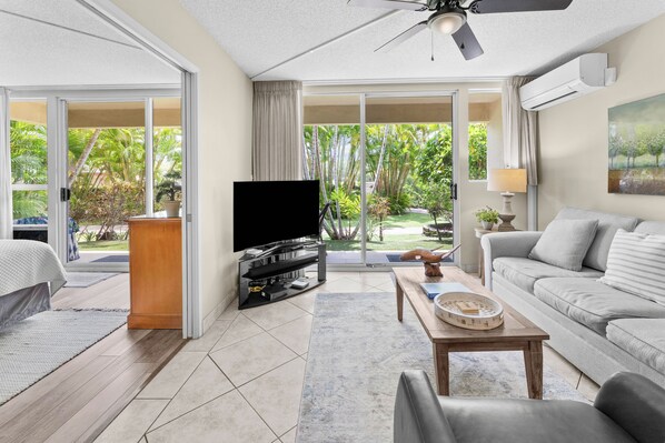 A spacious living room with a flat-screen TV, a sofa, a coffee table, and a ceiling fan.