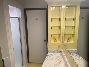 Kylpyhuone, jossa on valkoinen ovi, marmorinen taso ja keltainen laattaseinä, jossa on lasihyllyt.