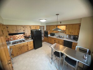 Eine Küche mit Holzausstattung, einem schwarzen Kühlschrank, Arbeitsplatten aus Edelstahl und einem Essbereich mit Tisch und Stühlen.