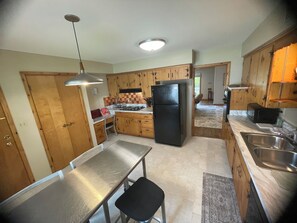 A compact kitchen with wooden cabinets, a stainless steel countertop, a black refrigerator, and a hanging light fixture. - Peaceful 2-bedroom brick Shorewood house near Lake Michigan beaches. (Shorewood)