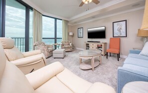 A spacious living room with a large window, a flat-screen TV, and a ceiling fan. - Phoenix Ix 607 2 Bedroom Condo (Orange Beach)