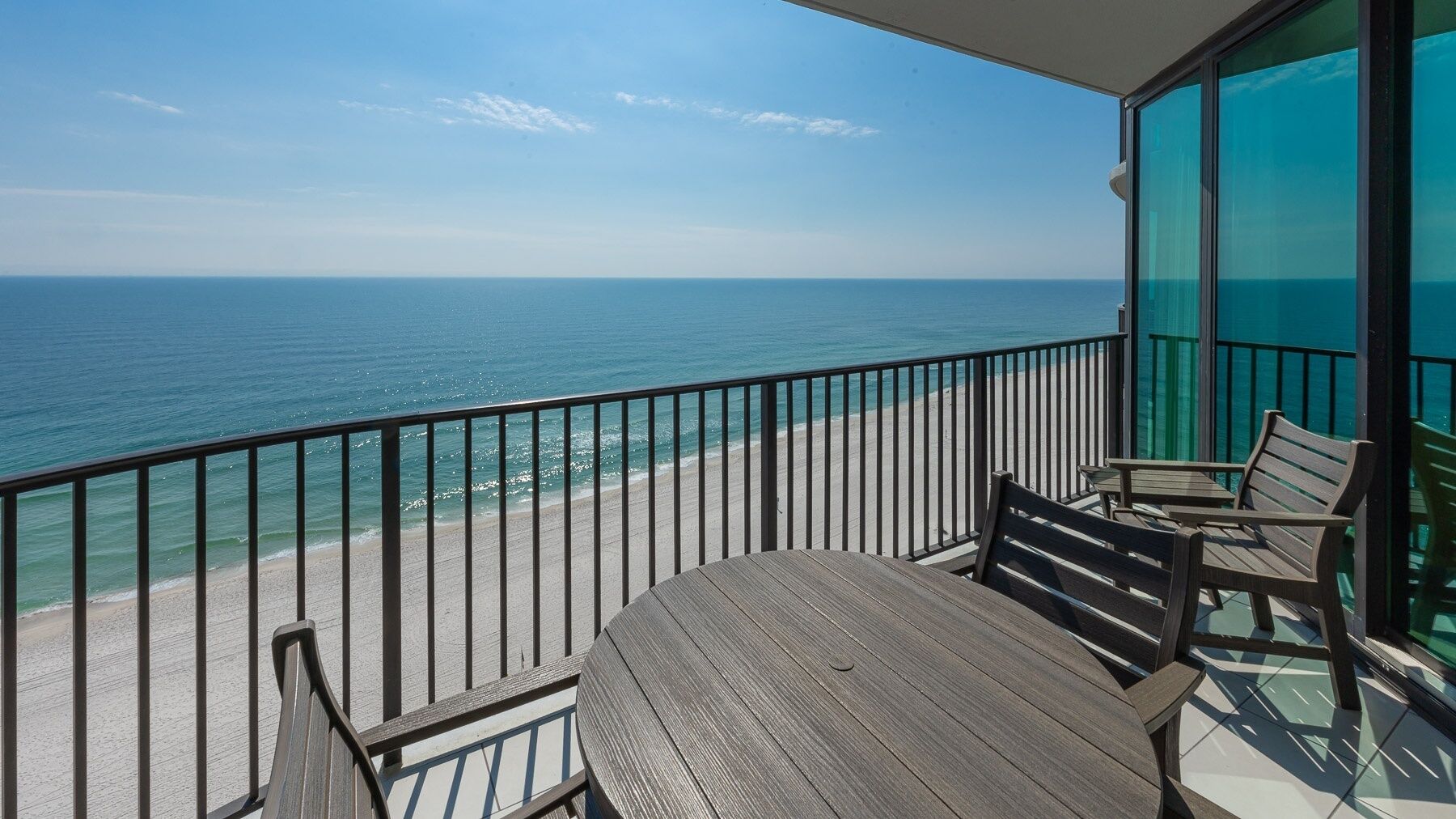 A balcony with a view of the ocean, a table, and chairs.