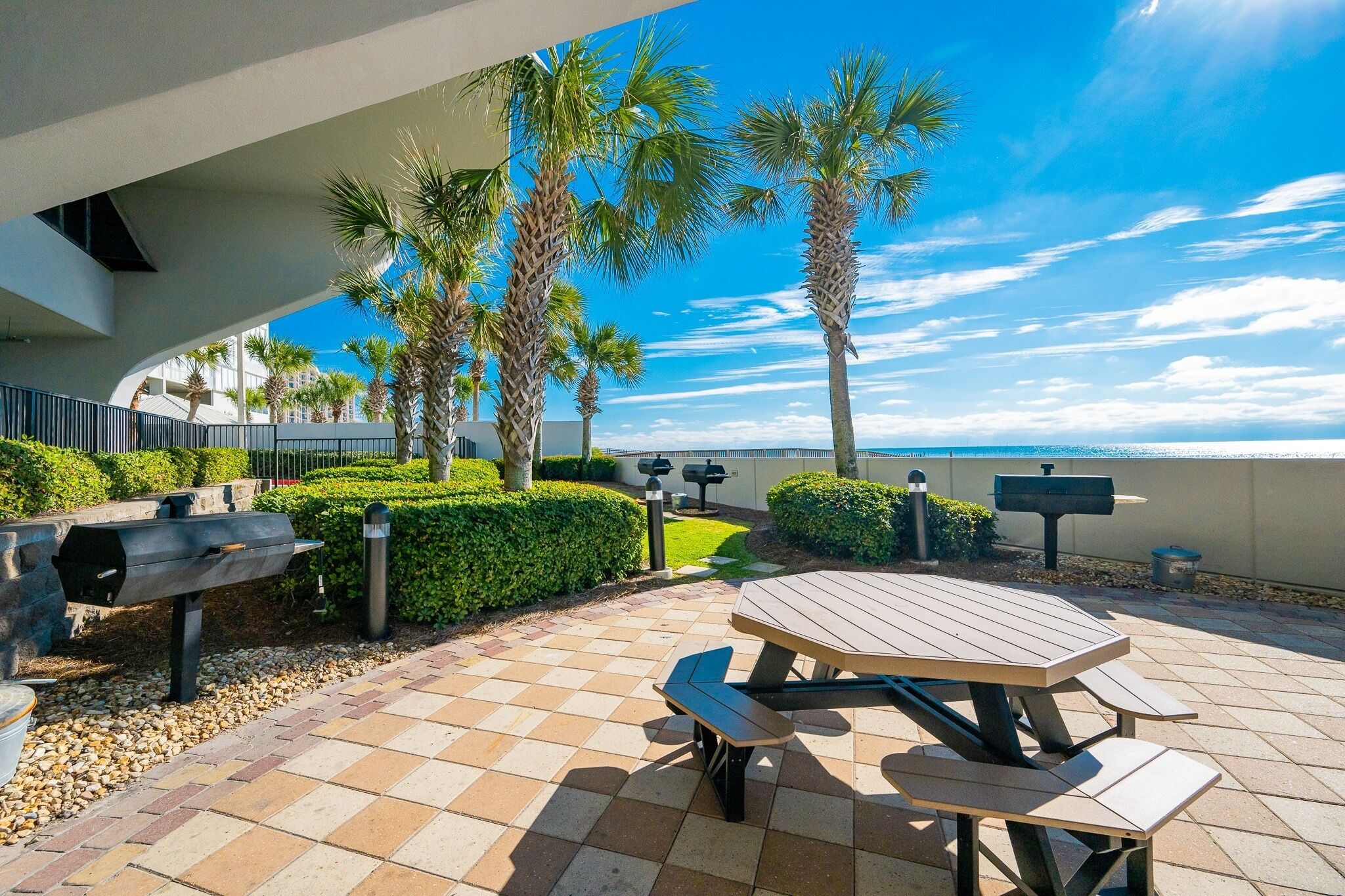 Un'area patio con tavolo da picnic, barbecue e palme.
