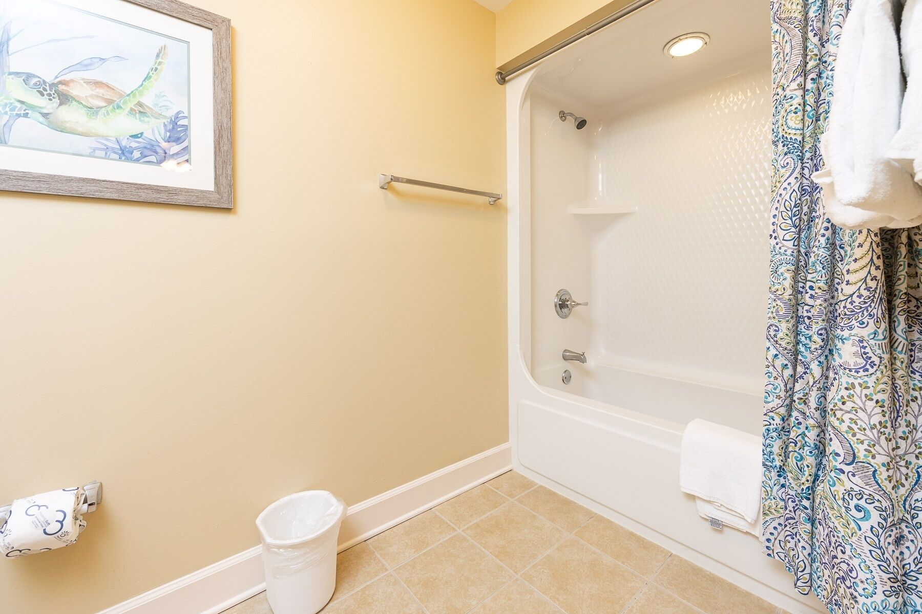 A bathroom with a bathtub, a shower, a toilet, a trash can, and a framed picture on the wall.