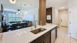 A modern kitchen with a central island, a built-in sink, and a dining area with a green table and chairs. - Beautiful Three Bed Condo, Minutes From Disney 3 Bedroom Condo (Kissimmee)