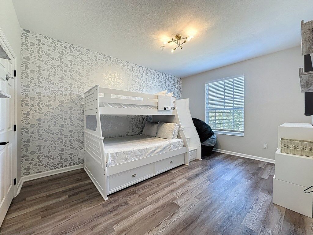 A child's bedroom with a bunk bed, patterned wallpaper, and a window with blinds.