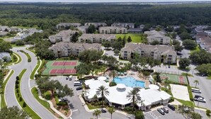 An aerial view of a residential area with apartment buildings, a swimming pool, tennis courts, and a curved road. - Beautiful Three Bed Condo, Minutes From Disney 3 Bedroom Condo (Kissimmee)