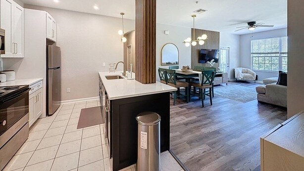 A modern kitchen with a central island, dining area with a table and chairs, and a living room with a sofa and a TV. - Beautiful Three Bed Condo, Minutes From Disney 3 Bedroom Condo (Kissimmee)
