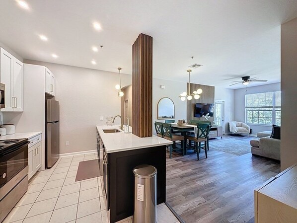 A modern kitchen with a central island, dining area with a table and chairs, and a living room with a sofa and a TV. - Beautiful Three Bed Condo, Minutes From Disney 3 Bedroom Condo (Kissimmee)