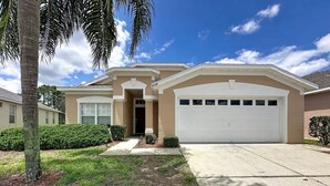 A single-story house with a garage, a front entrance, and a well-maintained lawn. - Whispering Palms - Luxury 4-Bedroom Pool Home Near 4 Villa (Kissimmee)