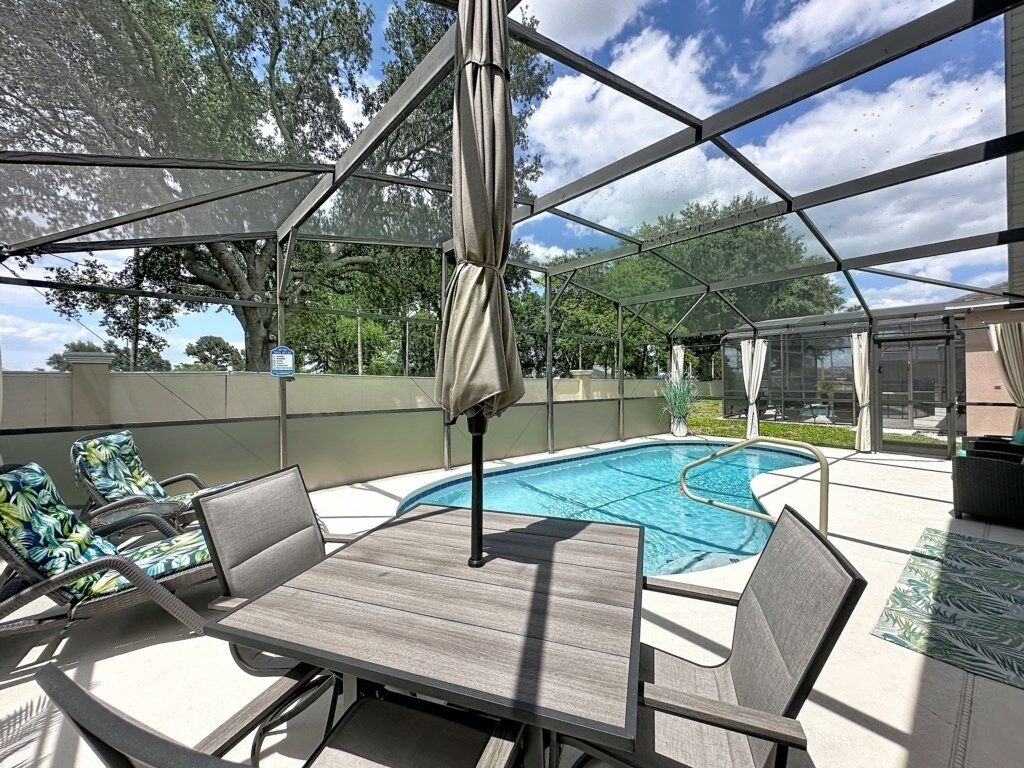 An outdoor patio with a pool, a table, and chairs.