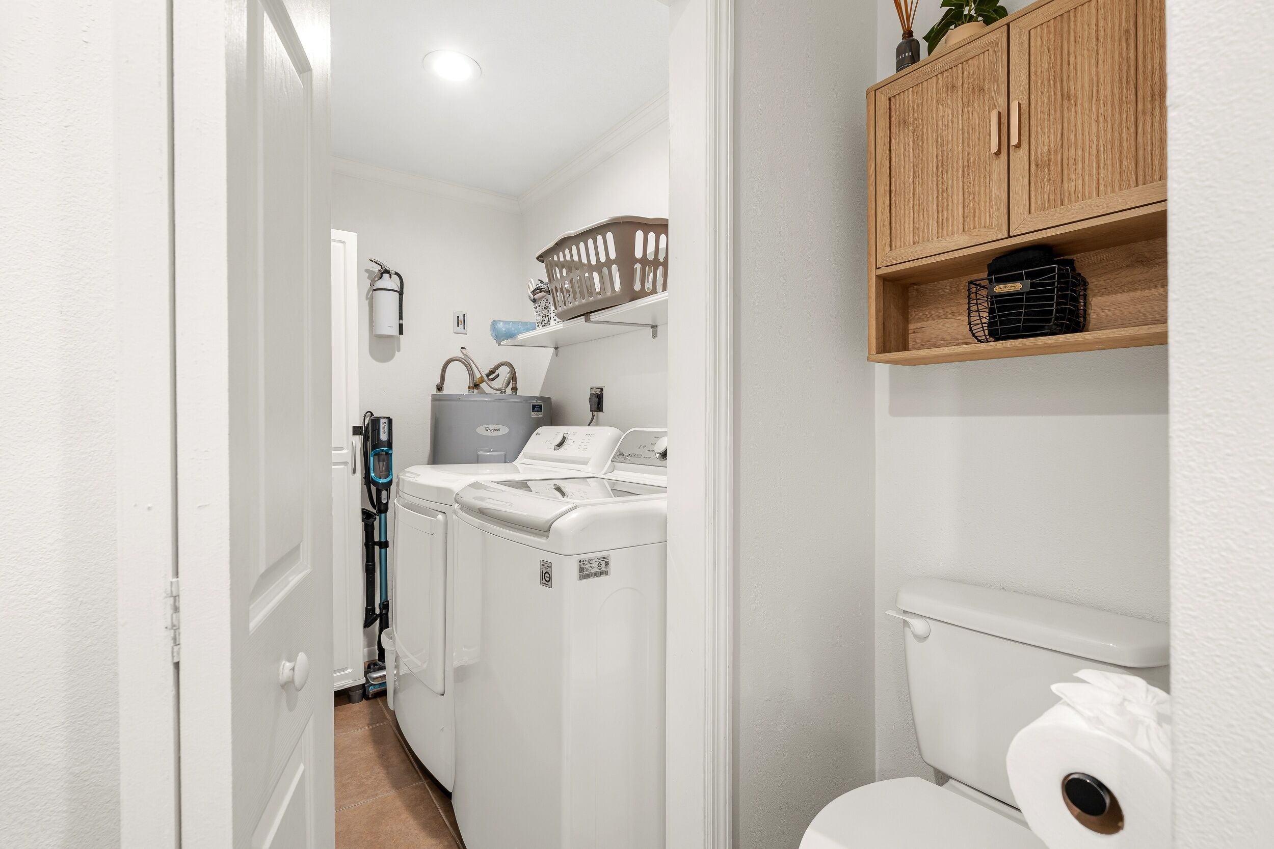 Un espace buanderie compact comprenant un lave-linge, un sèche-linge et une étagère en bois au-dessus des toilettes.