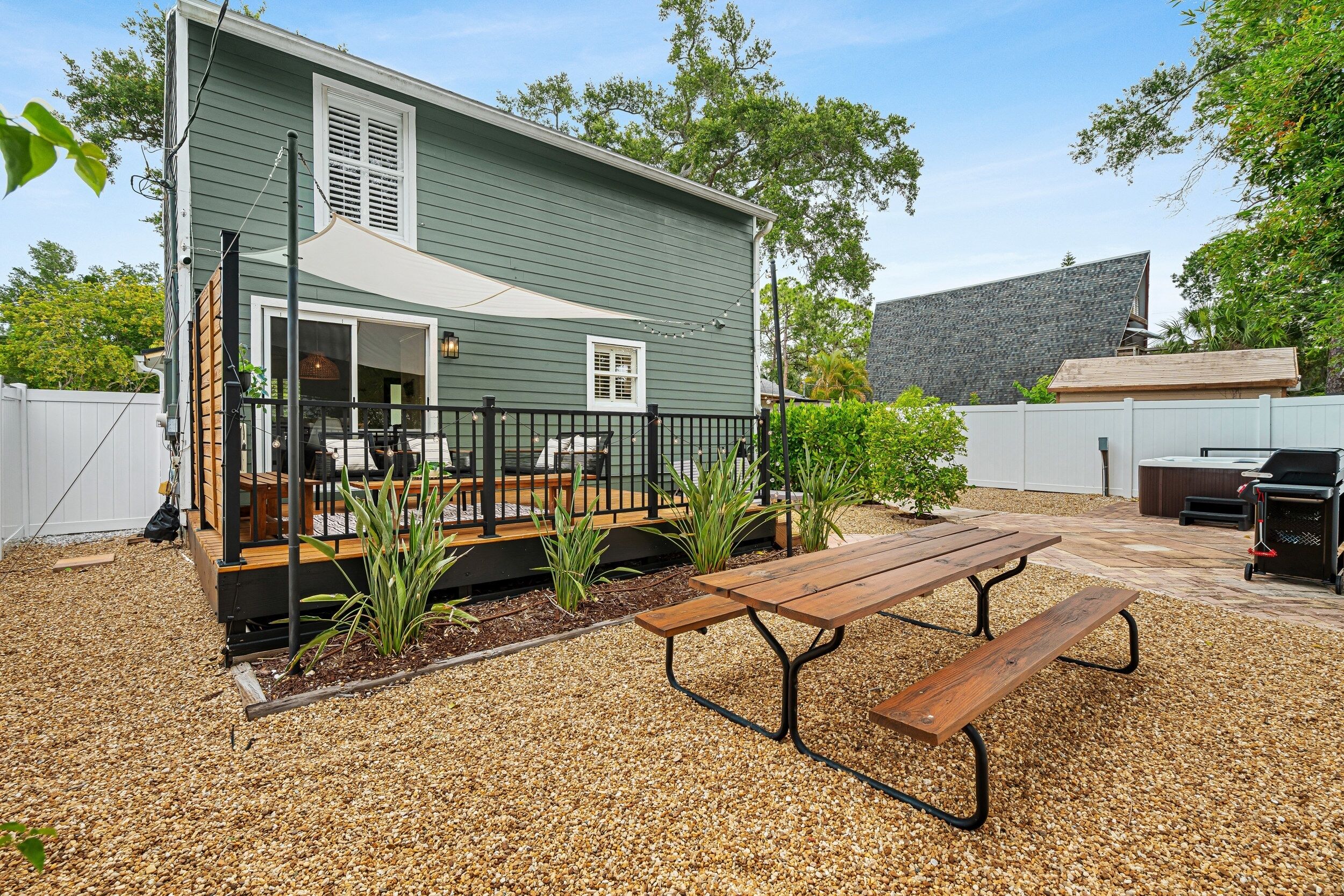 A house with a deck, a patio with a table and benches, and a barbecue area.