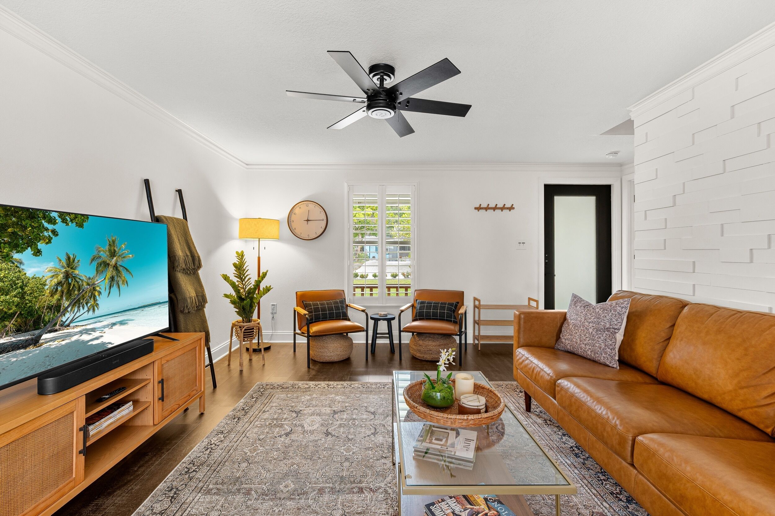Un salon équipé d’un téléviseur, d’un ventilateur de plafond, d’un canapé, d’une table basse et d’un coin repas avec des chaises.