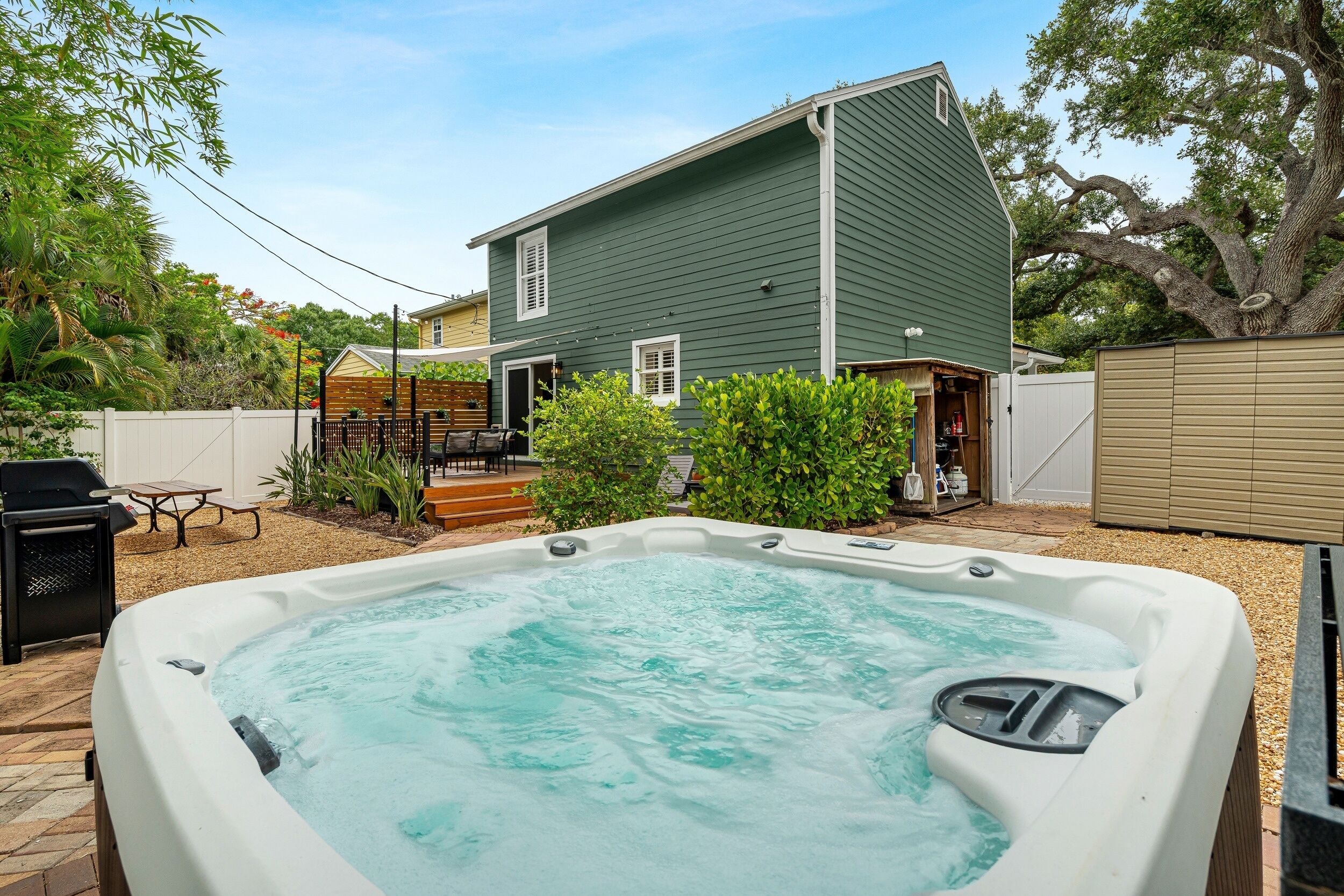 A backyard with a hot tub, a wooden deck, and a house.