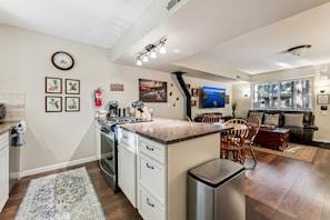 Eine moderne Küche mit einer zentralen Kochinsel, ein Essbereich mit Tisch und Stühlen sowie ein Wohnzimmer mit Sofa und Fernseher.