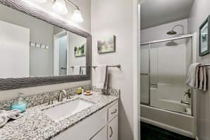 A bathroom with a granite countertop sink, a large mirror, a shower with a glass door, and a towel rack. - 1200w21 The Mountain Condo 2 Bedroom Condo (South Lake Tahoe)