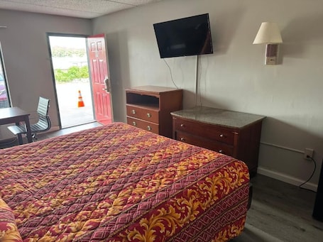A hotel room with a bed, a TV mounted on the wall, a desk, and a chair.. Regency Inn