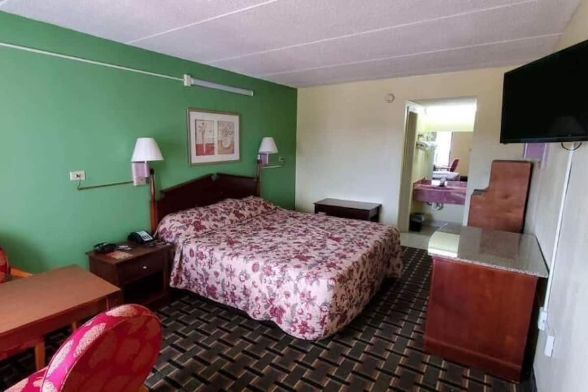 A hotel room with a bed, a desk, a chair, a TV, and a mirror.