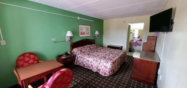 A hotel room with a bed, a desk, a chair, a TV, and a mirror. - Regency Inn (Riverdale)