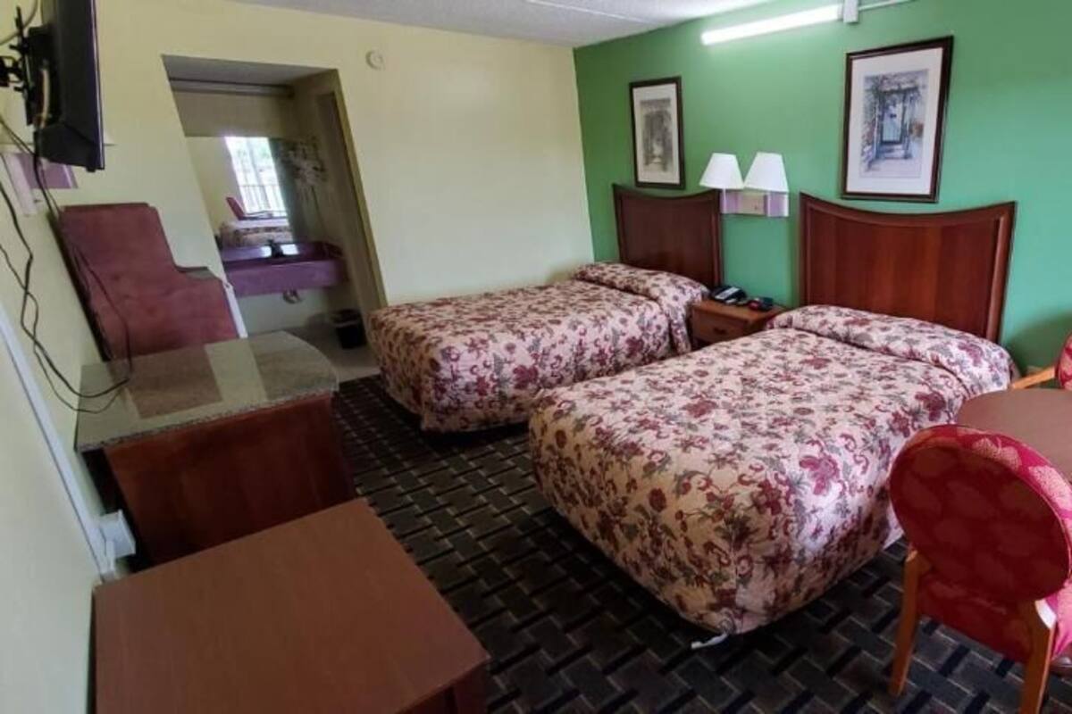 A hotel room with two beds, a desk, a chair, a television, and a window.