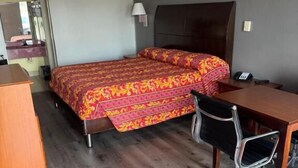 A hotel room with a bed, desk, chair, and a small wooden dresser. - Regency Inn (Riverdale)