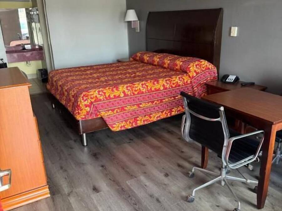 Een hotelkamer met een bed, bureau, stoel en een kleine houten dressoir.