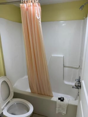 A bathroom with a bathtub, toilet, and shower curtain. - Regency Inn (Riverdale)