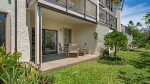 A two-story building with a balcony, a patio with chairs, and a well-maintained lawn. - Kauai Kahala At Poipu Kai 212 1 Bedroom Condo (Koloa)