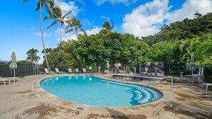 A swimming pool with lounge chairs and umbrellas, surrounded by palm trees and a stone wall. - Kauai Kahala At Poipu Kai 212 1 Bedroom Condo (Koloa)