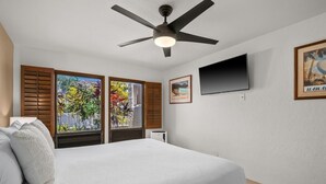 A bedroom with a bed, a ceiling fan, a TV, and a window with shutters. - Kauai Kahala At Poipu Kai 212 1 Bedroom Condo (Koloa)