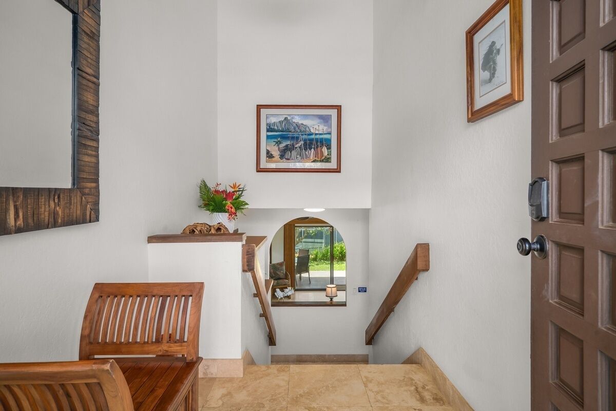 Una escalera conduce a un rellano con un cuadro enmarcado, un banco de madera y una puerta.