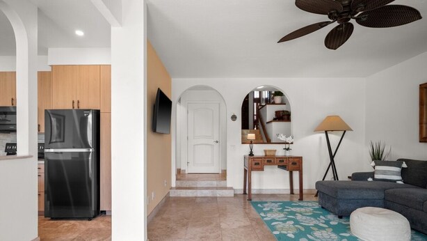 A modern kitchen with a refrigerator, a dining area with a table and chairs, and a living room with a sofa and a ceiling fan. - Kauai Kahala At Poipu Kai 212 1 Bedroom Condo (Koloa)