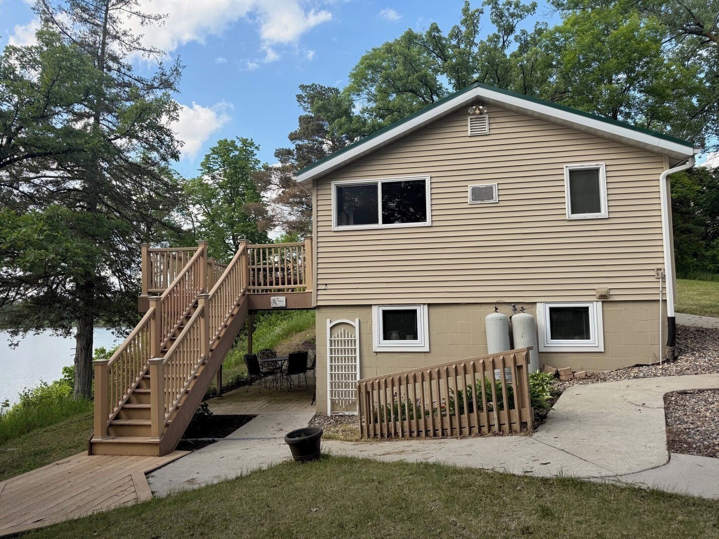 Une maison à deux étages dotée d’une terrasse en bois, d’un escalier et d’un petit espace patio.