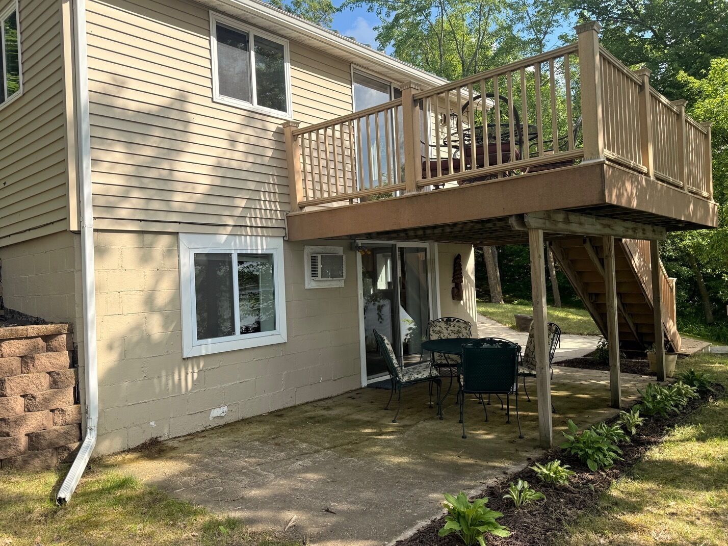 A two-story house with a deck, a patio with outdoor furniture, and a brick wall.