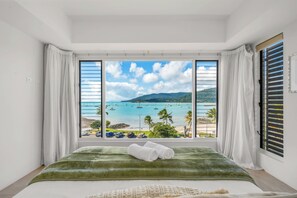 A bedroom with a large window offering a view of a beach and boats. - Airlie Beach Penthouse (Airlie Beach)