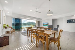 A spacious living area with a dining table, chairs, a TV, and a view of the sea. - Airlie Beach Penthouse (Airlie Beach)