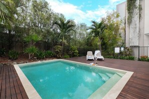 A rectangular swimming pool with a wooden deck, surrounded by lush greenery and a fence. - Airlie Beach Penthouse (Airlie Beach)