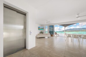 A spacious living area with a sliding door, a flat-screen TV, a sofa, and a dining area with chairs. - Airlie Beach Penthouse (Airlie Beach)