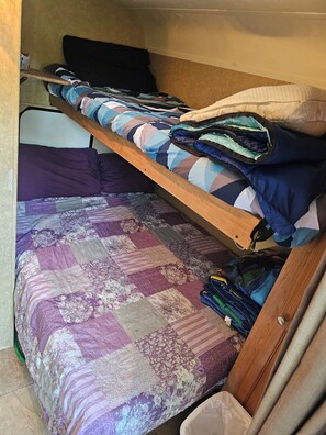 Un lit superposé avec une couvre-lit matelassé et un tiroir de rangement contenant des vêtements pliés.