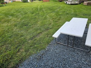 Une table de pique-nique posée sur une base de gravier, entourée d’une zone herbeuse.